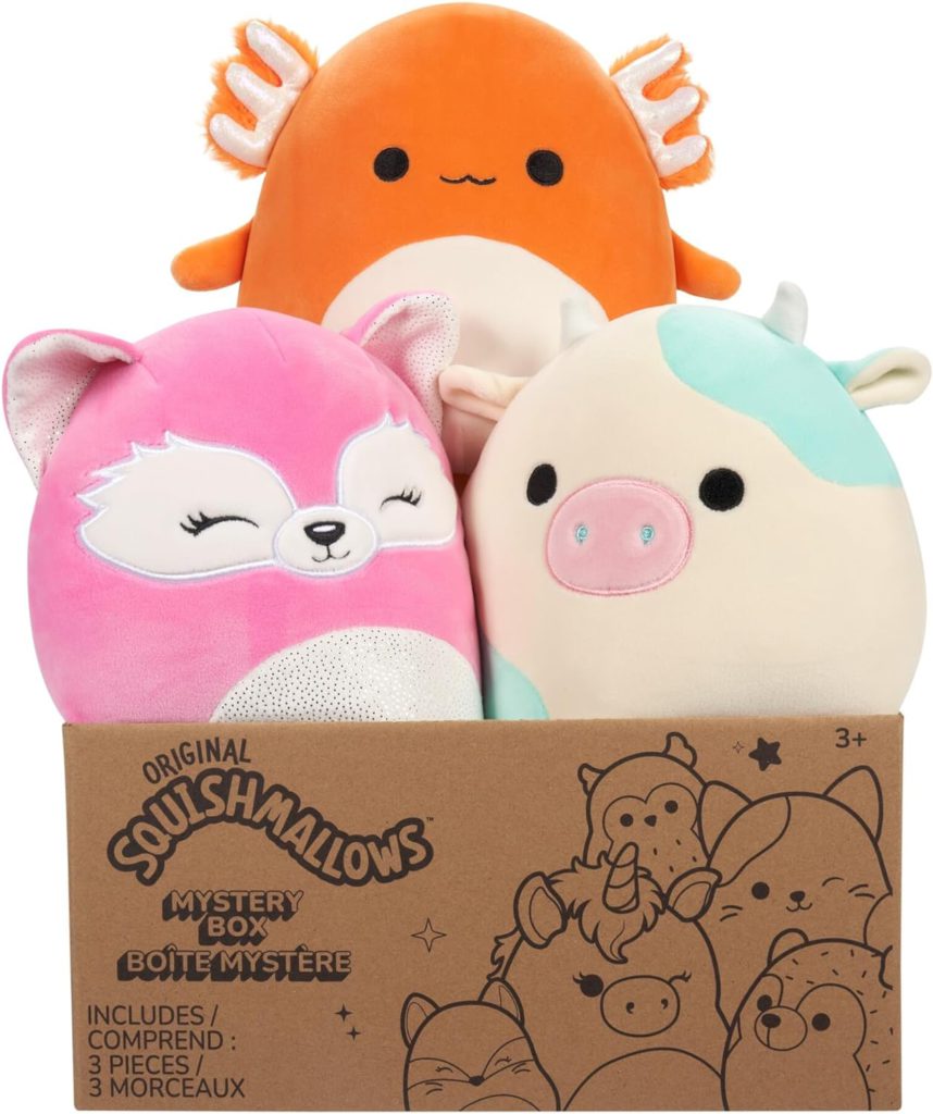 A mystery pack of squishmallows is shown with three stuffed animals bursting out of a cardboard box. The image shows a fox, cow, and lizard however the contents vary.