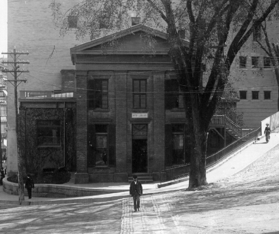 This photograph of the original building was taken some time during the late nineteenth century from the steps of the Norwich City Hall. A man crosses the street toward the camera. The same tree from the line drawing is still towering above the building.