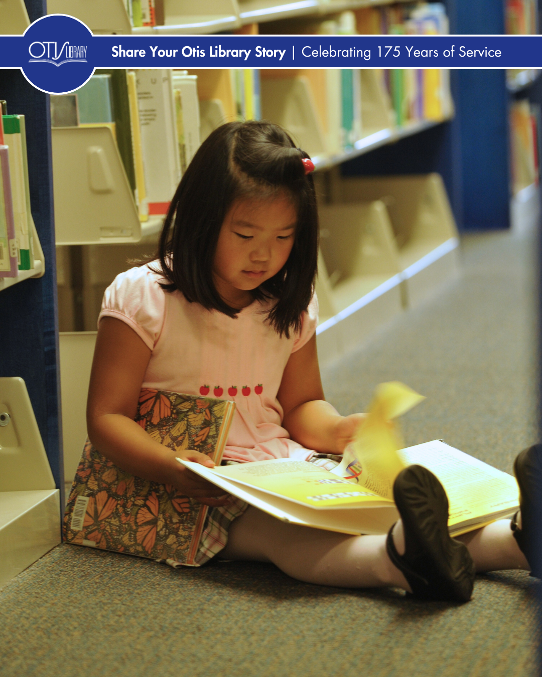A young girl sits on the floor flipping through a book. Behind her are rows of shelves with books in the children's department.