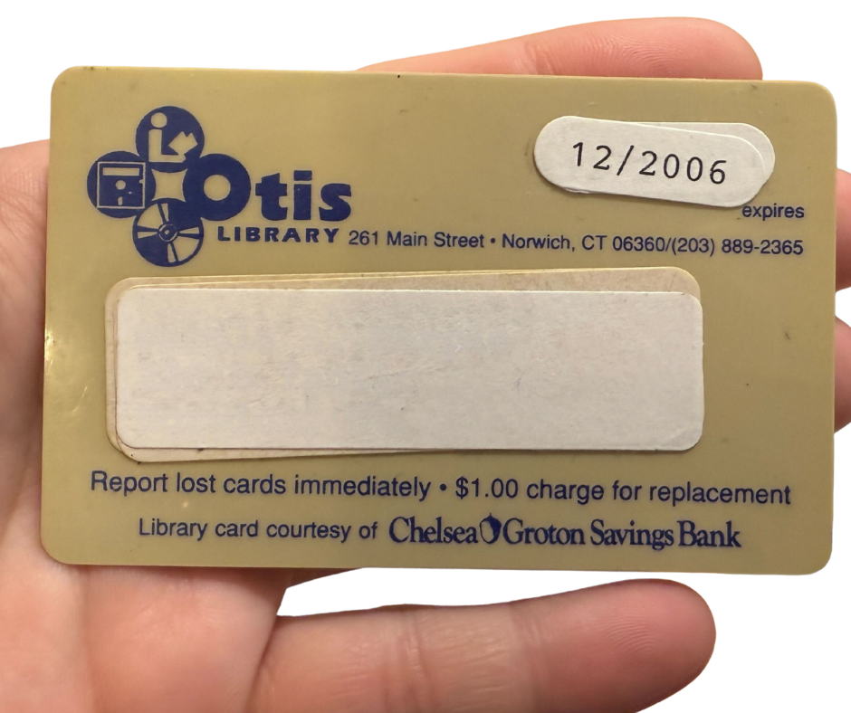 A hand holds a library card. The card is clearly well loved with stickers and faded plastic. It has an outdated logo on it. The logo features the public library symbol, a CD, and a floppy disc. The expiration date says 2006, though the logo is much older than that.